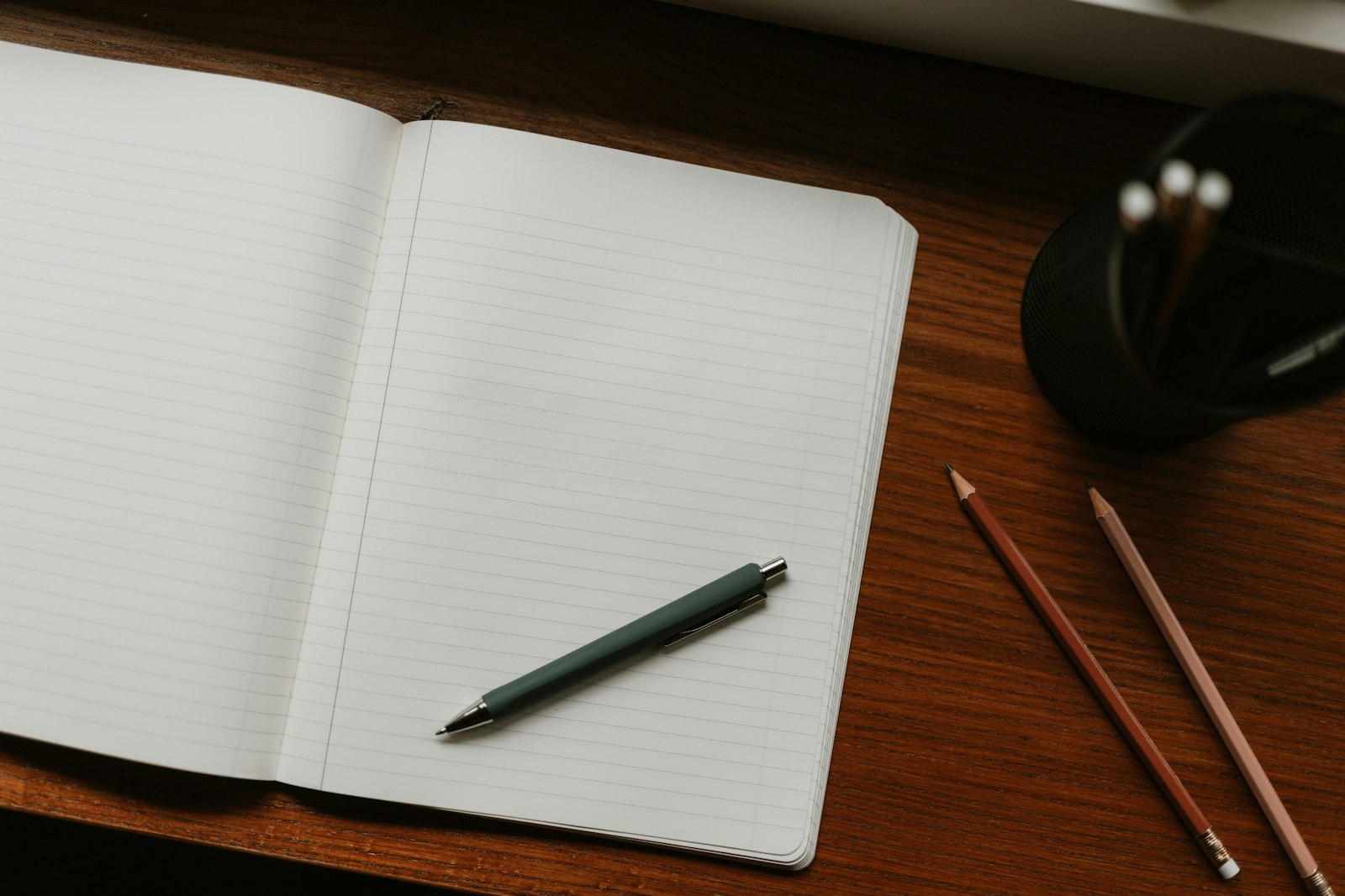 An open lined notebook with a pen and pencils on a wooden desk